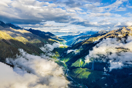 Majestic mountain range with deep valley shrouded in fluffy white clouds under bright sky in Sichuan, China.