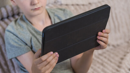 Young boy holding digital tablet sitting on couch at home. Child studying online, playing games or watching video content on modern portable device indoors. Technology and education concept. ( © Тетяна Хіміченко