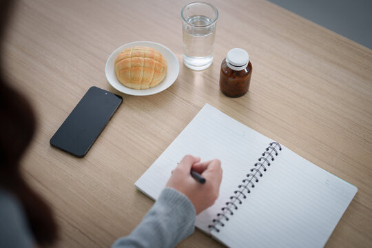 High angle view of person writing in notebook at wooden desk with breakfast