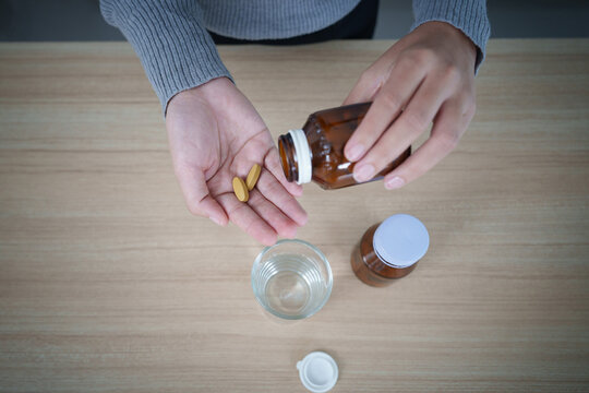 High angle view of hands pouring yellow pills into palm for daily vitamin supplement routine