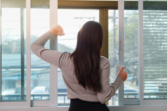 Asian woman holding coffee mug standing by window during morning routine at home