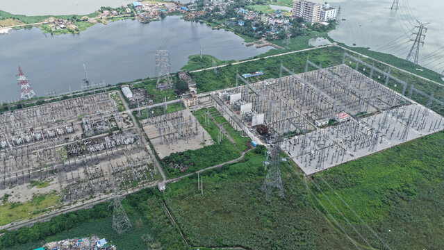 Aerial view of a large electrical power substation with high voltage transmission towers and transformers situated near a riverbank in Dhaka, Dhaka Division, Bangladesh.