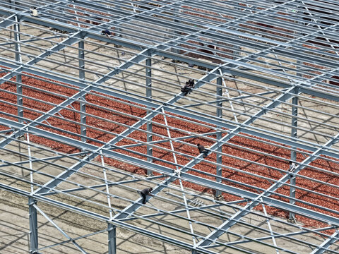 Aerial view of construction workers installing steel beams on a large industrial building frame in Dhaka, Dhaka Division, Bangladesh.