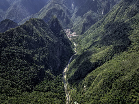 Aerial view of the town of Aguas Calientes nestled in a deep valley surrounded by lush green mountains and the Urubamba River in Aguas Calientes, Cusco, Peru.