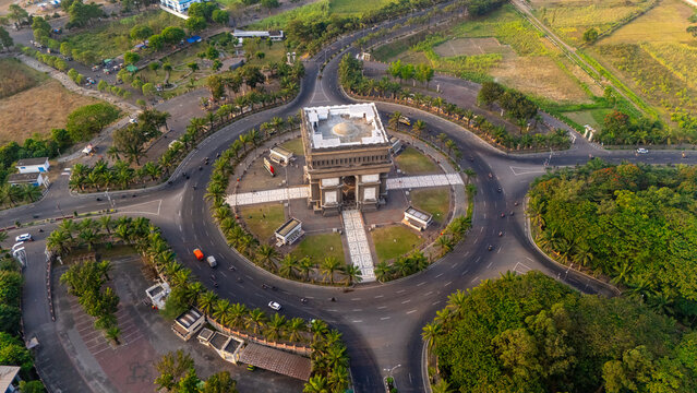Aerial view of the Simpang Lima Gumul Monument situated in a large roundabout surrounded by palm trees and lush green spaces in Kediri, East Java, Indonesia.
