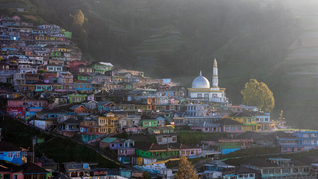 Aerial view of the colorful hillside village featuring a prominent mosque with a silver dome nestled among terraced slopes in Kaliangkrik, Central Java, Indonesia.