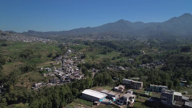 Aerial drone footage of rural village and green vegetable farmland with Mount Panderman background in Pujon, Malang