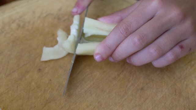 Hands slicing green bell pepper on wooden cutting board. Close-up shot.