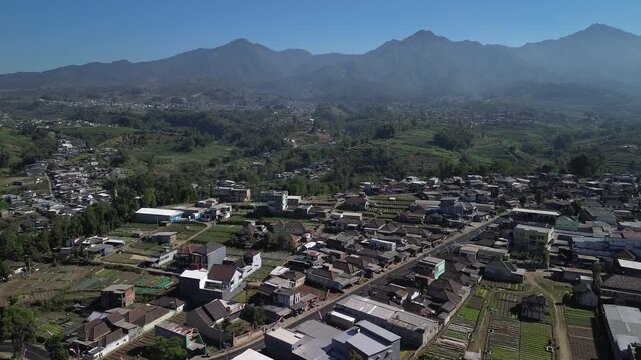 Aerial drone footage of rural village and green vegetable farmland with Mount Panderman background in Pujon, Malang