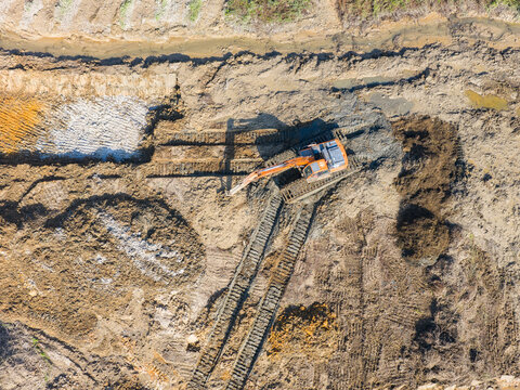 Excavator on earthmoving at construction site, aerial view.