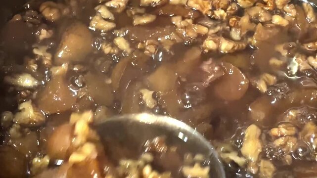 Cooking pear jam with walnuts in a large pot, stirring with a spoon, sweet fruit preserve.