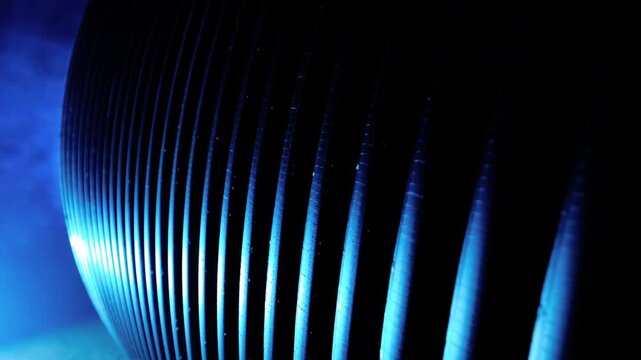 Close-up motion of curved parallel metal fins in studio environment showing stationary slats with intensifying cool-blue rim highlights along lower-left edges while valleys remain deep black