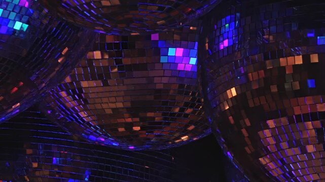 Multiple mirrored spheres, closely captured, reflect amazing light spectacle. Bright blues, greens, oranges, and purples dance across myriad faceted surfaces, creating vibrant club ambiance at night.