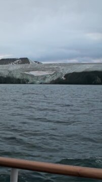 Experience the breathtaking majesty of Arctic glaciers meeting the dark, choppy sea. A peaceful voyage across frigid waters under an overcast sky, showcasing nature's raw power.