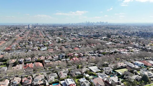 Aerial view of the residential neighborhood in Malvern East during winter, featuring bare deciduous street trees and the Melbourne city skyline on the distant horizon in Australia. Established suburb
