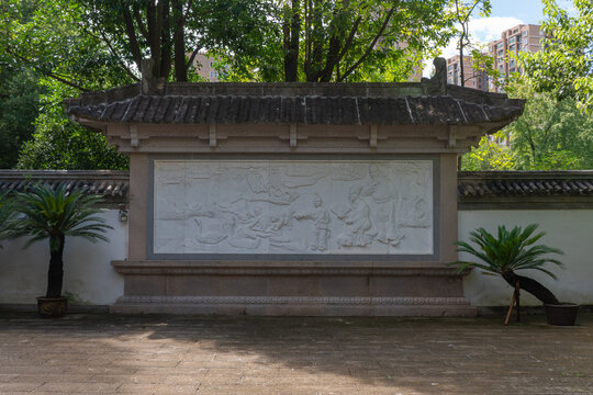 Traditional Chinese stone relief carving depicting historical figures and waterfowl, set in a courtyard with tiled roof and potted cycads