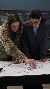 Vertical shot of young adult Caucasian female soldier and female specialist analyzing tactical map in command center. Footage is perfect for defense industry and security marketing