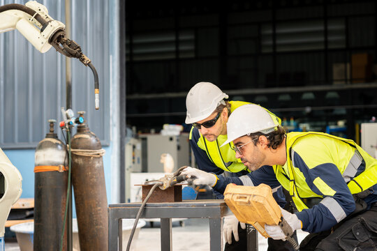 Engineers working with robotic welding arm and control unit in factory, Technicians inspecting automated welding machine and metal part in plant, Workers team operating robotics automation assembly
