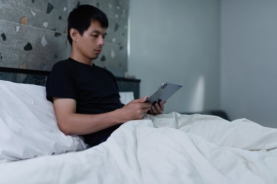 Young Man Sitting in Bed Using Tablet in Minimalist Bedroom