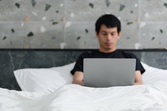 Person Using Laptop While Sitting on Bed Under White Blanket
