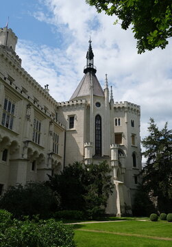 High-quality travel stock photo of Hluboka chateau chapel exterior. Elegant neo-gothic spires, stained glass windows and stone turrets surrounded by green trees in Czechia.