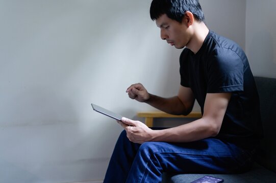 Thoughtful man using tablet while sitting on sofa indoor space