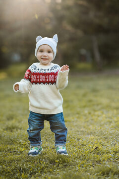 Kid boy 1 year old wearing knitted sweater and hat walking in autumn park. Childhood.