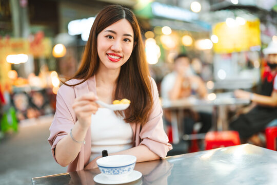 Smiling face traveler woman eating dessert at street food market tasty asia menu tour nightlife in Chinatown Bangkok city