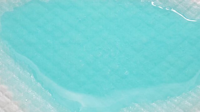 Absorbent hygiene pad absorbing turquoise liquid, close-up demonstration of superabsorbent polymer performance