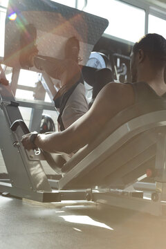 African American man pressing leg-press footplate gripping handles in gym wearing tank top