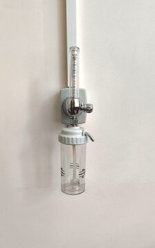 Medical oxygen flowmeter with a transparent humidification bottle, wall-mounted in a hospital.