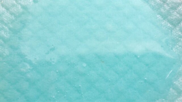 Blue liquid being absorbed by white quilted absorbent pad, close-up demonstration of superabsorbent polymer performance
