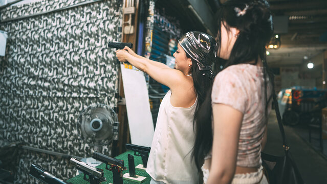 Two young asian women enjoy playing bb gun game at shooting booth