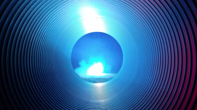 Centered eye-level view through corrugated cylindrical tunnel toward circular opening showing visible emergence and intensification of bright plume and smoke at floor level near exit