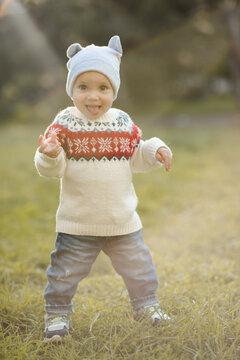 Kid boy 1 year old wearing knitted sweater and hat walking in autumn park. Childhood.