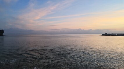 Obraz premium Pastel sunrise over the calm sea and distant coastline in Brittany, France.