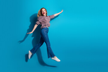 Naklejka premium Young woman jumping in a blue studio background in casual sweater and jeans showcasing happiness fashion and lifestyle vibe