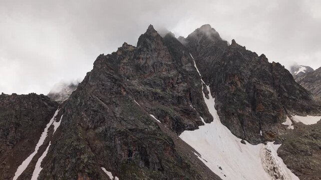 Steep rocky mountain peak with snow and moving clouds