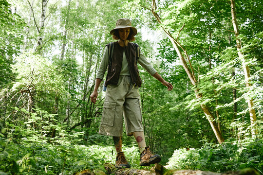 Caucasian young adult woman hiking in forest, balancing on fallen tree trunk. Image represents outdoor recreation and is suitable for ecotourism marketing, low angle shot
