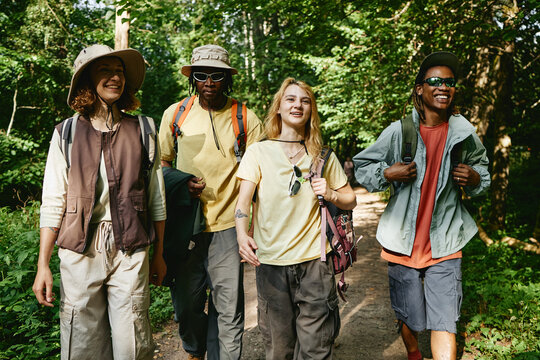 Diverse young adult friends hiking in forest, walking on trail and smiling. Image represents outdoor recreation and eco tourism, suitable for active lifestyle marketing campaigns