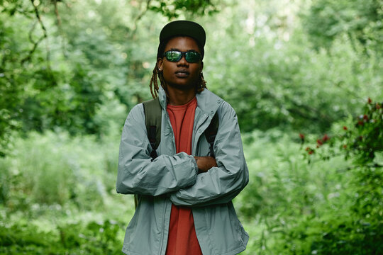Portrait of young Black man with dreadlocks hiking in forest with arms crossed. Image represents outdoor recreation and is suitable for eco tourism marketing campaigns
