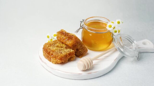 Honey in jar with honeycomb and flowers on white board