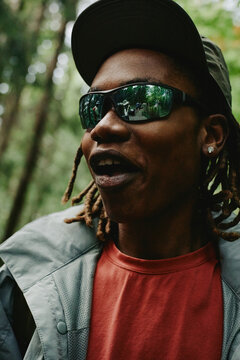 Vertical shot of young adult Black man with dreadlocks hiking in forest with friends reflected in sunglasses. Image ideal for outdoor gear marketing and adventure travel campaigns