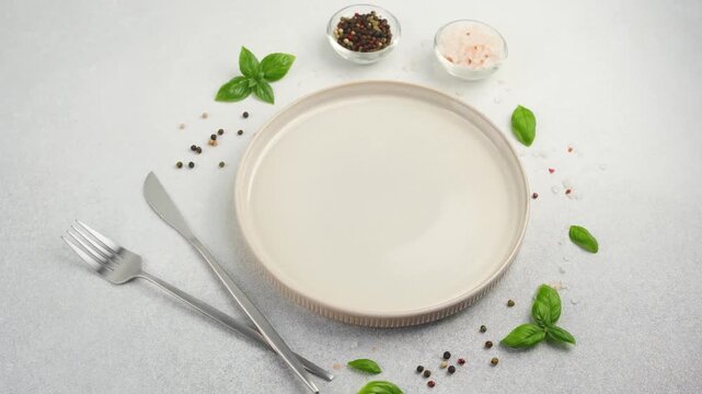 Empty plate with fork and knife surrounded by basil and peppercorns on a textured background
