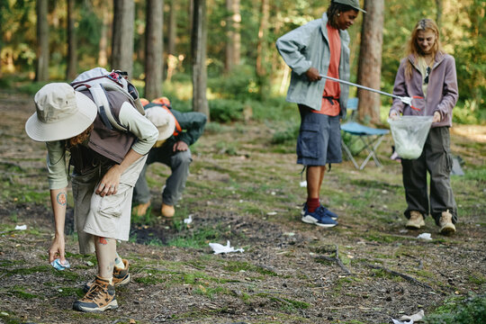 Diverse young adult friends picking up litter in forest, promoting environmental conservation. Image suitable for eco friendly campaigns and community volunteering advertisements