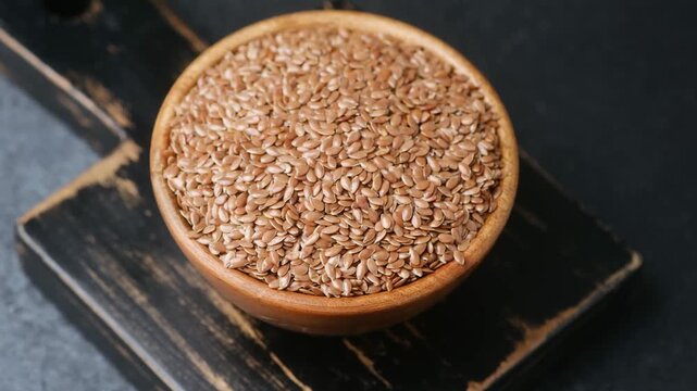Wooden bowl filled with flax seeds on a textured background