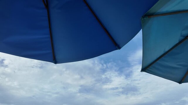 Low angle view of blue beach umbrellas set against a cloudy blue sky