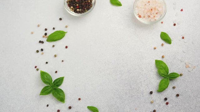 Fresh basil leaves and assorted peppercorns with pink salt scattered on a light gray background