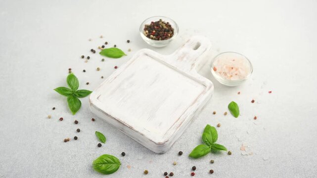 White cutting board with basil, peppercorns, and pink salt on a light background