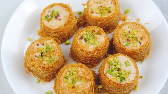Kataifi nests filled with cream and topped with chopped pistachios on a white plate